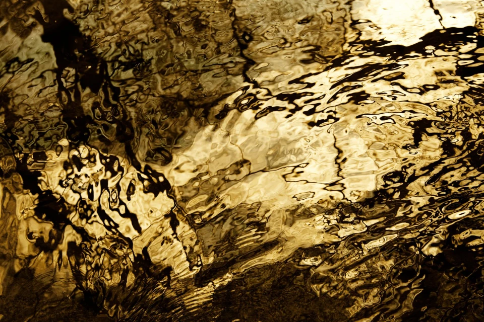 Abstract golden water surface with dark reflections creating a unique and shimmering pattern, excellent for backgrounds and textures.