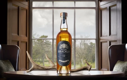 Bottle of Royal Brackla whisky on a dark wood table with deer antlers against a large window and armchairs