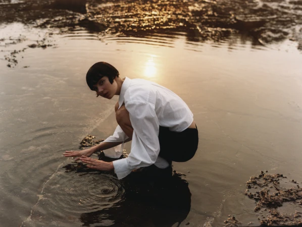 Woman in white shirt crouching and touching rippling water at sunset by photographer Darren Mcdonald