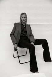 Monochrome portrait of a blonde woman wearing a tailored blazer and trousers while seated on a chair.