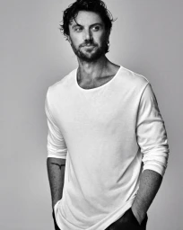 Monochrome portrait of a man with dark hair wearing a white long-sleeve t-shirt against a plain light grey background