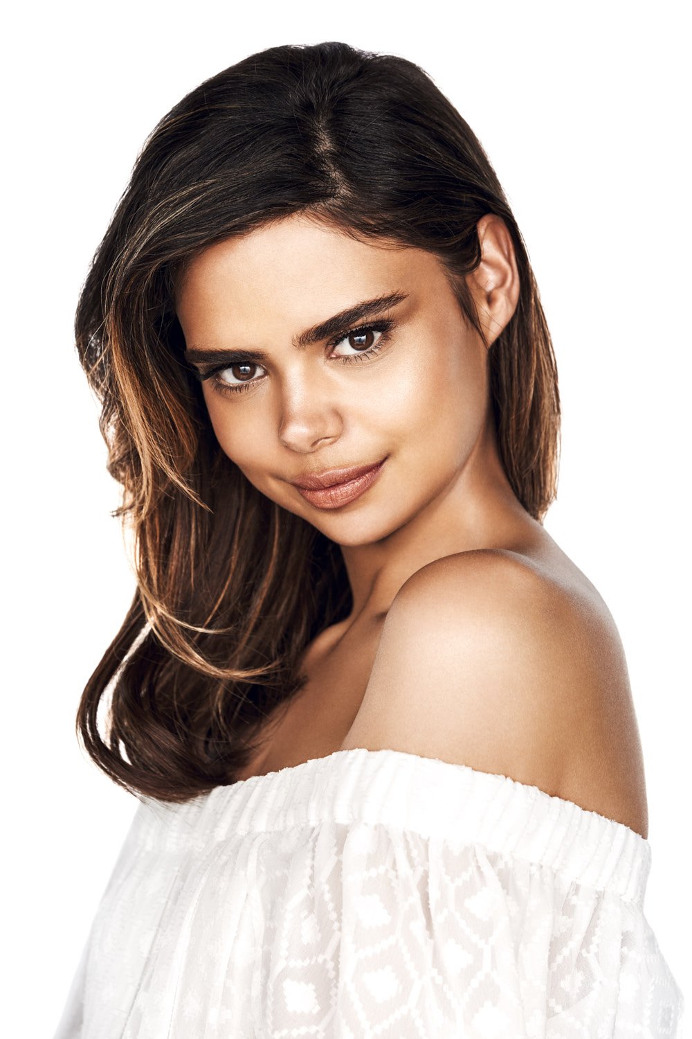 Portrait of a young adult woman with brunette ombre hair, wearing a white peasant blouse, smiling softly against a white background.