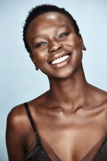 Smiling African woman portrait on blue background. Young adult female with dark hair and visible teeth poses in dark top.