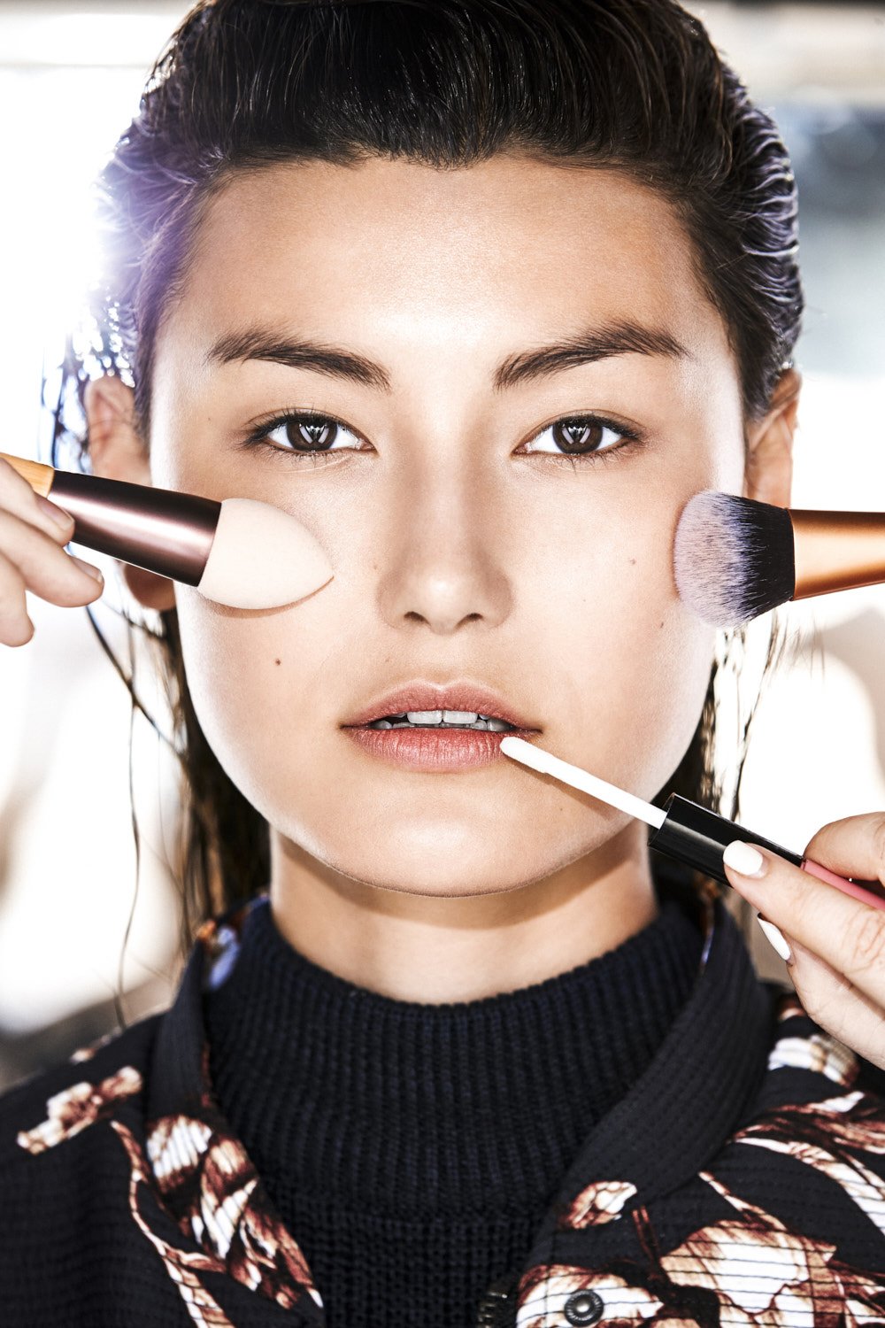 Asian woman getting makeup applied with brushes. Close-up beauty shot with neutral skin tone and natural makeup for skincare or cosmetics.