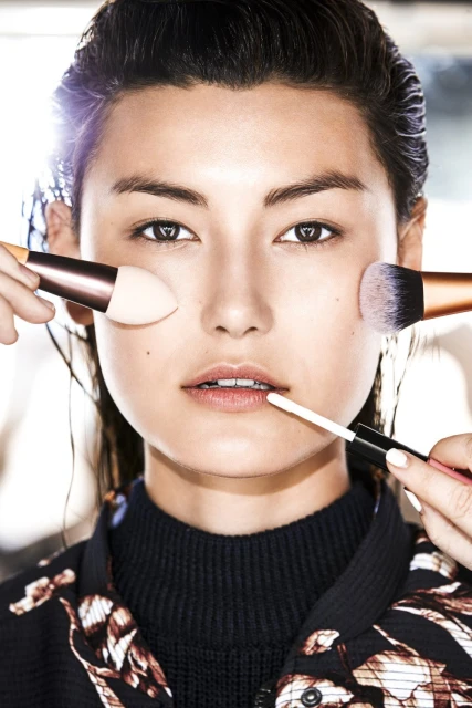 Asian woman getting makeup applied with brushes. Close-up beauty shot with neutral skin tone and natural makeup for skincare or cosmetics.