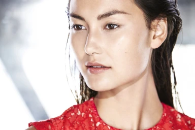Close-up portrait of a woman with wet dark hair wearing a red lace dress against a bright background