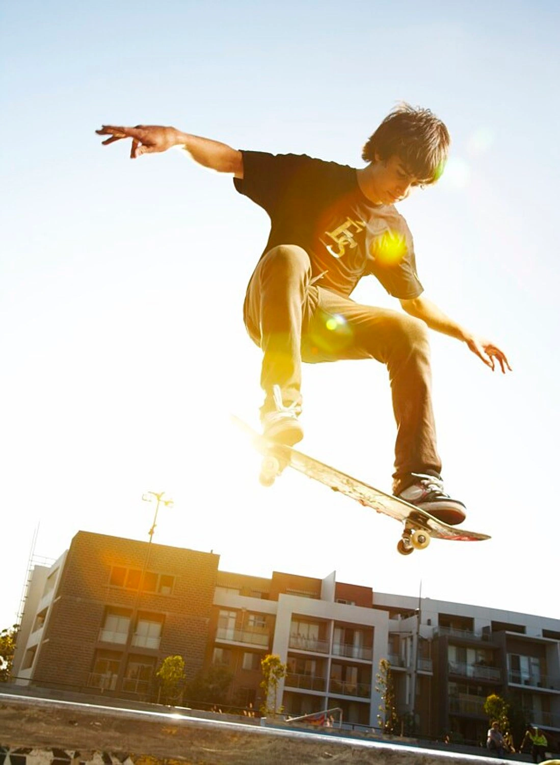 Young skater airborne on a skateboard against a bright sky above urban architecture by Paul Suesse
