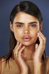 Close-up portrait of a woman with wet dark hair holding her hands to her face against a dark blue background by Paul Suesse