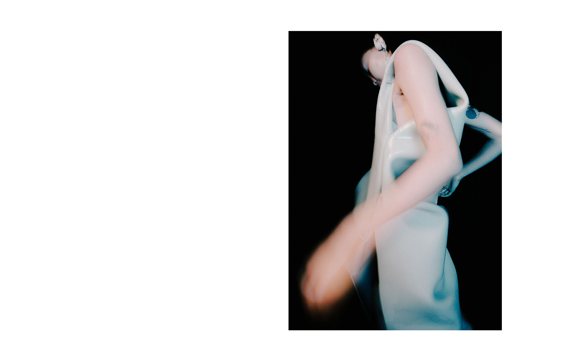 Woman in flowing white gown strikes a pose against a dark background, creating a dramatic contrast and sense of ethereal beauty.