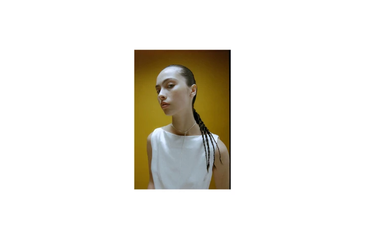 Portrait of a woman wearing a white top and silver necklace against a mustard yellow background