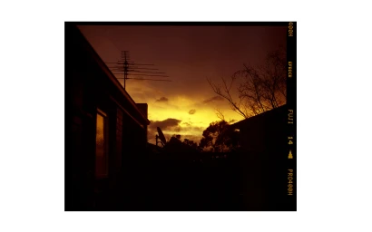 Analog photograph of a twilight sky with a bright yellow horizon framed by dark silhouetted rooftops and television antennas.