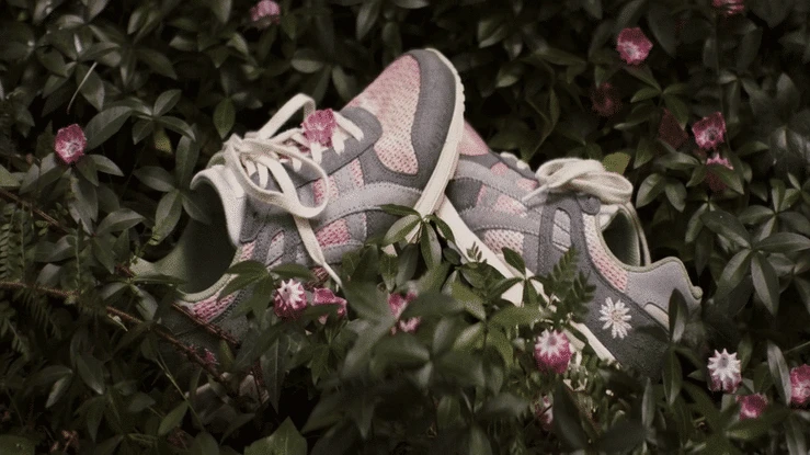 Close-up of gray and pink sneakers surrounded by green leaves and pink flowers, evoking a natural and organic aesthetic.
