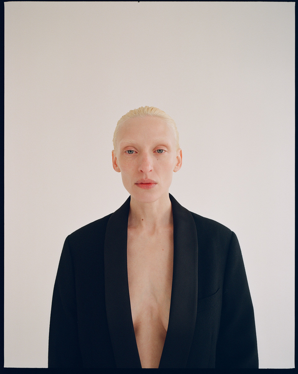Close-up studio shot of an adult woman with blonde hair, wearing a black blazer against a white background, focusing on beauty and fashion.