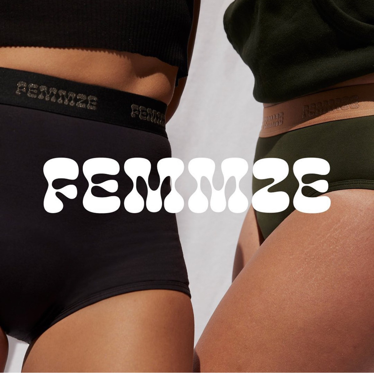 Two women pose wearing black and olive-green underwear with visible branding against a neutral backdrop in a studio fashion shot.