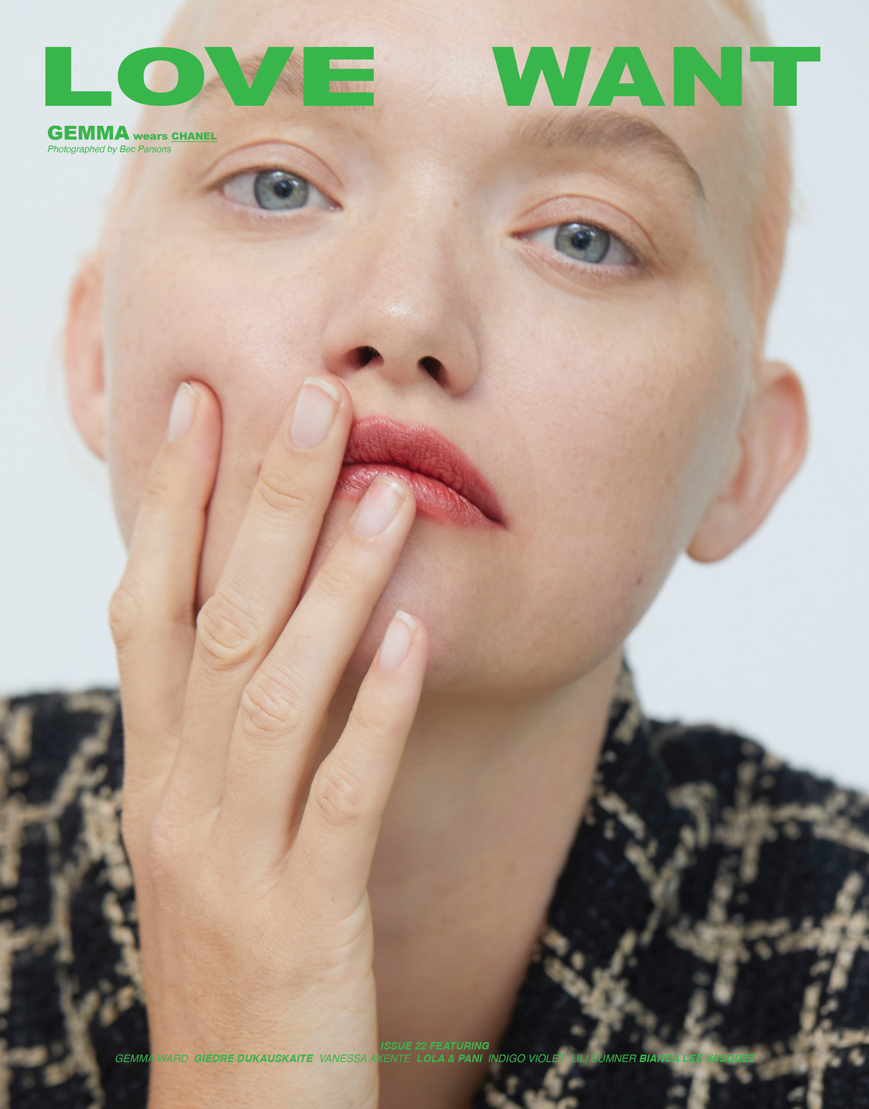Close-up portrait of a fair-skinned adult female fashion model with a buzzcut, wearing a tweed jacket with bright green typography.