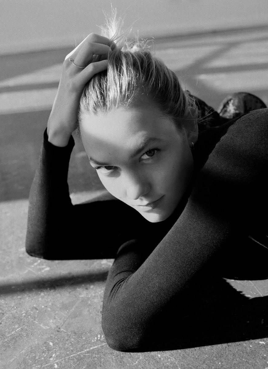 Monochrome portrait of a woman wearing a dark top with her hand in her hair, photographed by Bec Parsons.