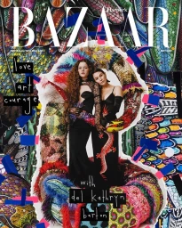 Two women posing in black gowns before a vibrant, highly textured multicolored sculptural backdrop