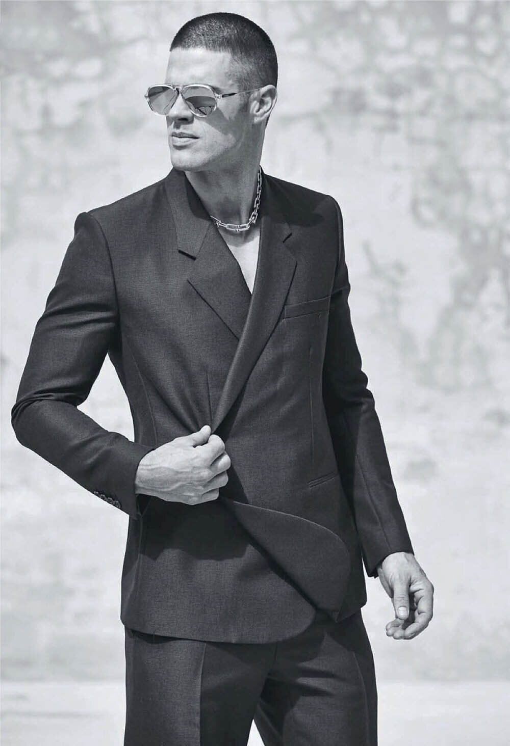 Monochrome portrait of a man wearing aviator sunglasses and a dark tailored suit jacket, styled by Grant Pearce.