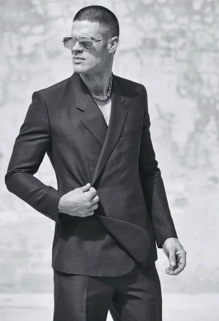 Monochrome portrait of a man wearing aviator sunglasses and a dark tailored suit jacket, styled by Grant Pearce.