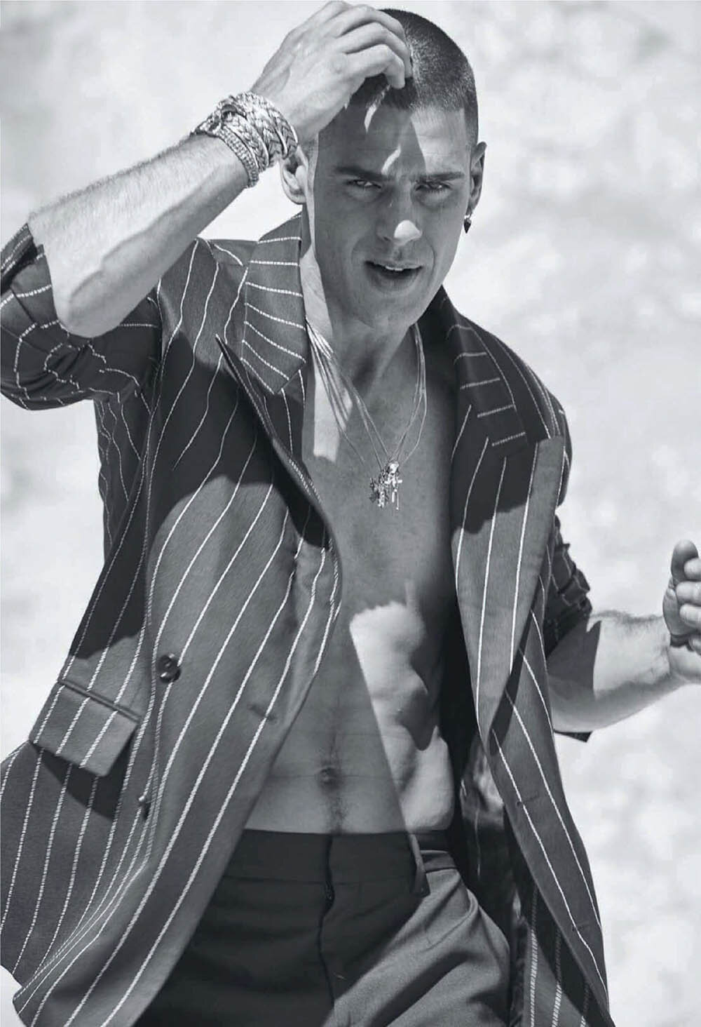 Striking black and white portrait of a male model wearing a pinstripe blazer, posing outdoors with hand near his hair.