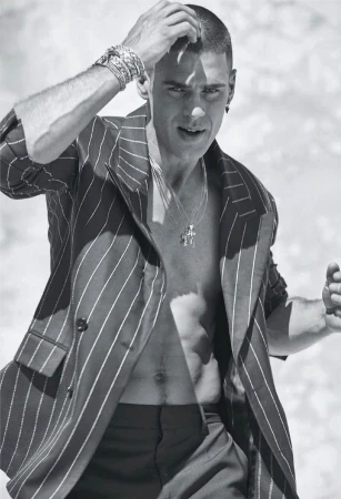 Striking black and white portrait of a male model wearing a pinstripe blazer, posing outdoors with hand near his hair.