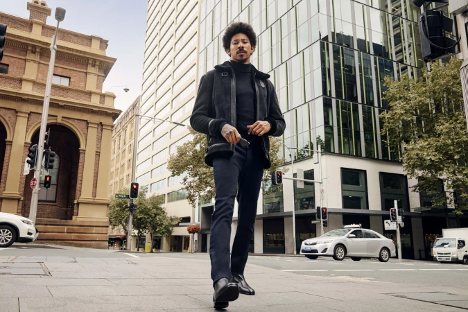 Man with afro hair wearing a black shearling jacket and turtleneck walking on a city street styled by Grant Pearce