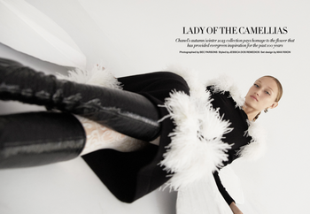 Fashion editorial shot of a female model in a black and white outfit with feathered details posing against a bright white background.