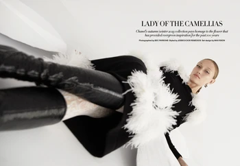 Fashion editorial shot of a female model in a black and white outfit with feathered details posing against a bright white background.