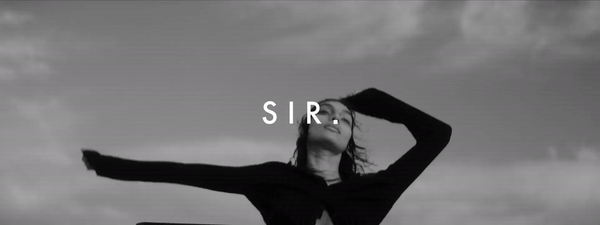 Monochrome portrait of adult female with serious expression against a cloudy sky, wearing dark clothing. Text overlay 'SIR.' is visible.
