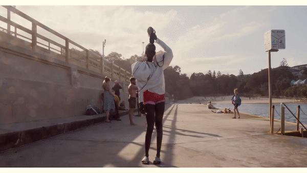 Fashion-forward video collage featuring a runway model in avant-garde clothing juxtaposed with beachgoers on a sunny pier.