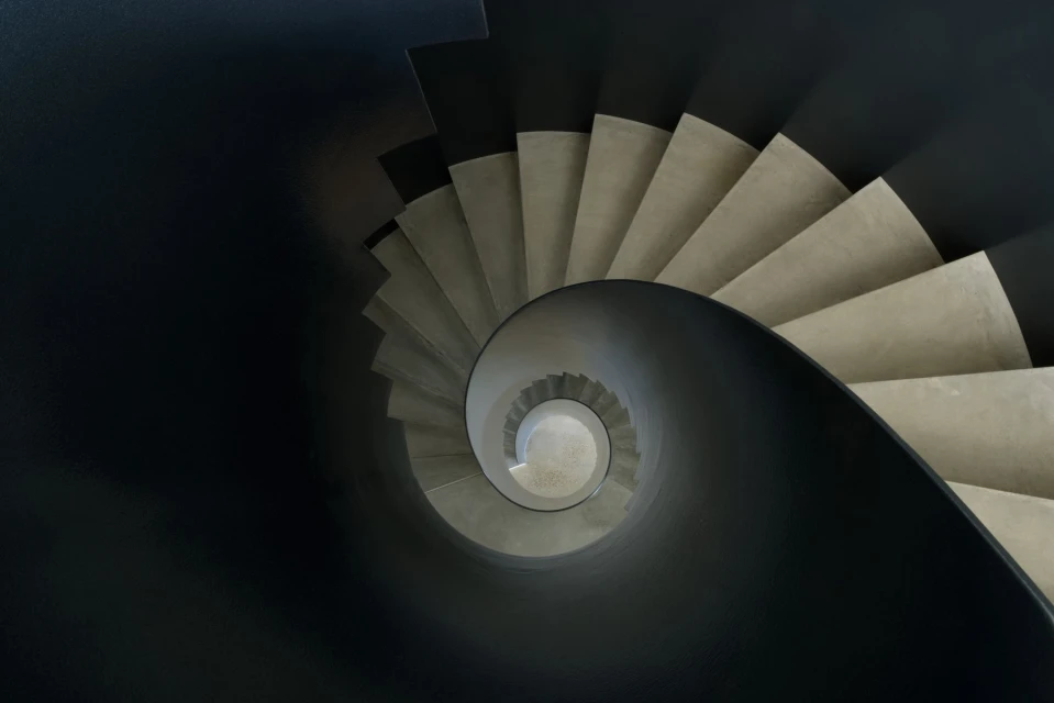Looking down at a spiral staircase with concrete steps and a dark gray bannister winding down to the center of the frame.
