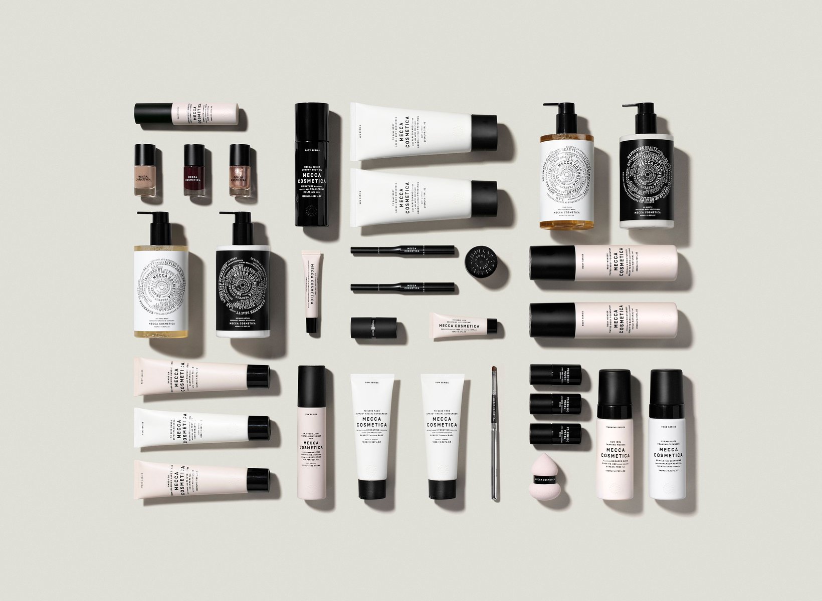 Flat lay of Mecca Cosmetica skincare, makeup, and beauty products in white, black, gold, and pink against a neutral backdrop.