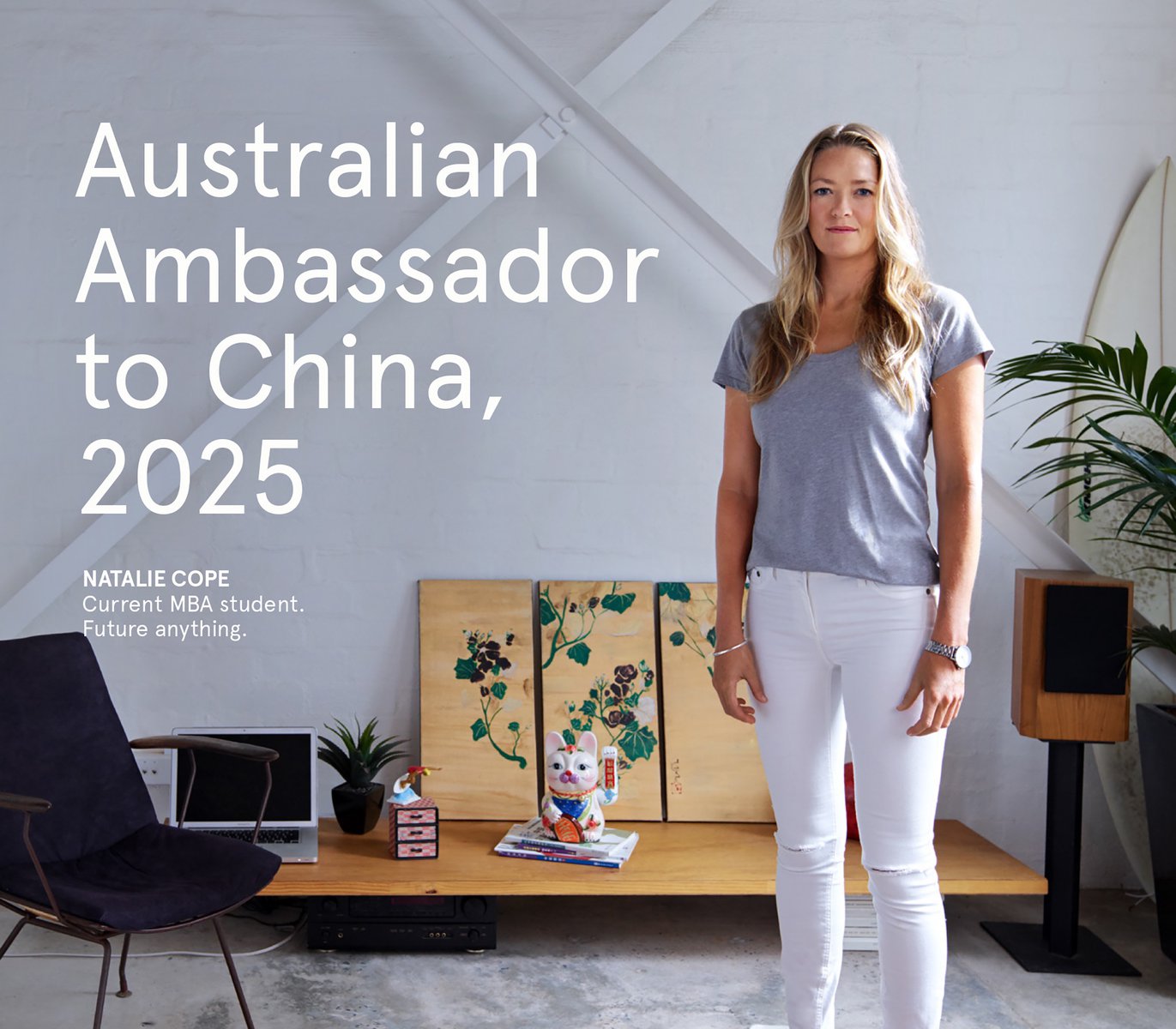 Blond woman in a gray t-shirt and white jeans stands in a modern interior with white walls and minimal decor and natural light.