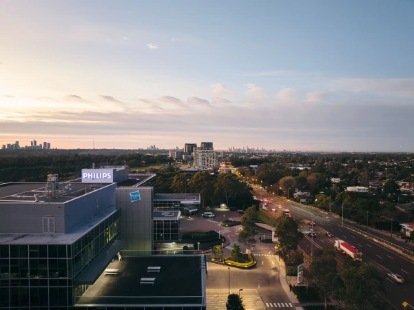High-angle view of a modern building complex with 'Philips' signage on the roof, set against an urban skyline and a sunset sky.