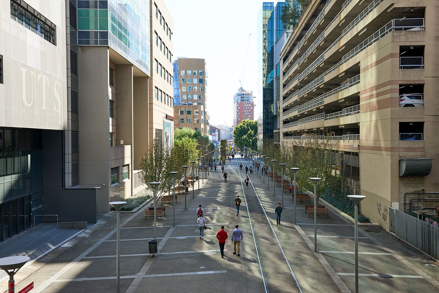Urban street scene with a pedestrian walkway, modern architecture, and people walking along the path on a sunny day, creating a vibrant city view.