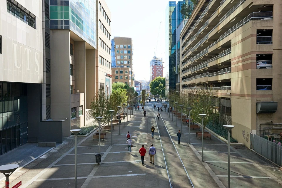 Urban street scene with a pedestrian walkway, modern architecture, and people walking along the path on a sunny day, creating a vibrant city view.