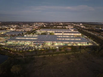 Aerial dusk view of a large commercial logistics warehouse with illuminated loading docks and parking lot in Sydney.