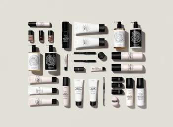 Flat lay of cosmetic bottles, tubes, and skincare products arranged on a pale grey seamless background