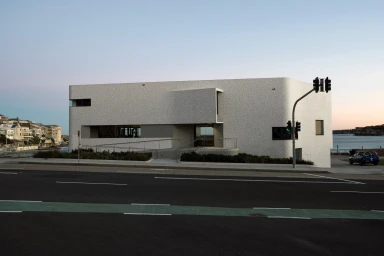 Modern white building exterior with curved corners overlooking a street with traffic lights under a clear sky
