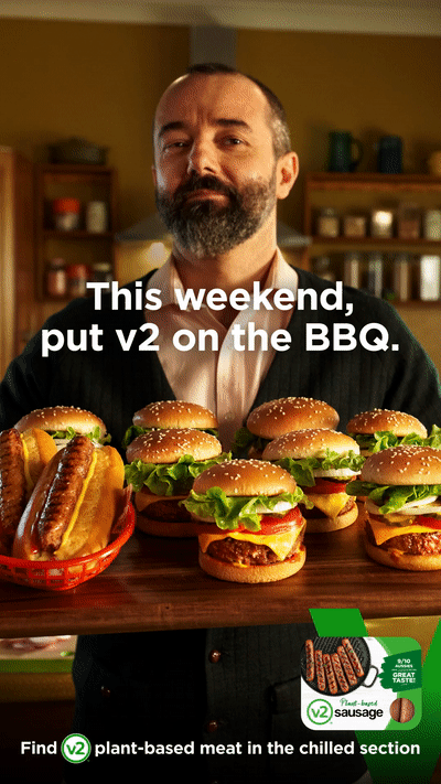Eye-level shot of a bearded man holding a tray filled with plant-based burgers and hotdogs, promoting a BBQ meat alternative.