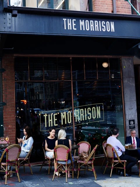 Exterior shot of The Morrison restaurant in an urban setting, featuring people seated at outdoor tables and the restaurant's facade.