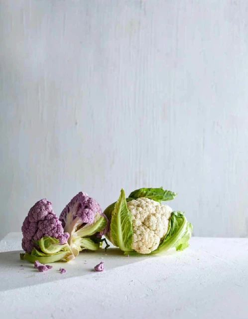 Still life of purple and white cauliflower heads on a white surface against a bright white background with a shallow depth of field.