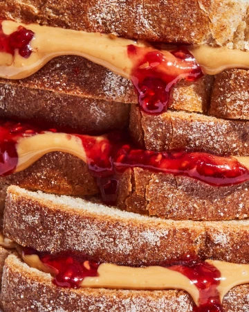 Close-up of a layered peanut butter and jelly sandwich featuring raspberry jam dripping down the sides of whole wheat bread slices.