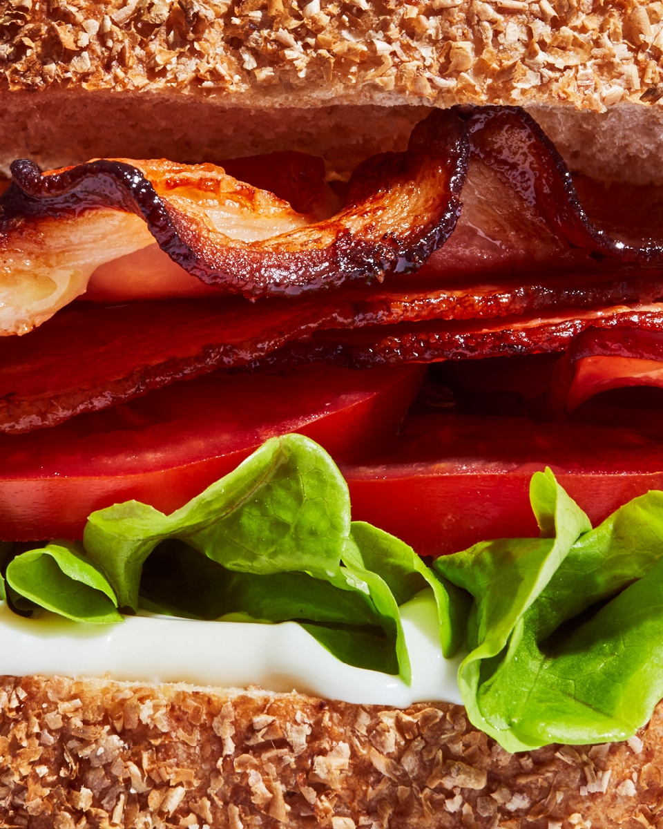 Close-up of a bacon, lettuce, and tomato (BLT) sandwich featuring crispy bacon, fresh lettuce, ripe tomatoes, and multigrain bread.
