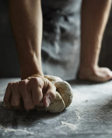 Close-up of hands kneading dough on a dark floured surface captured by Con Poulos in Sydney.