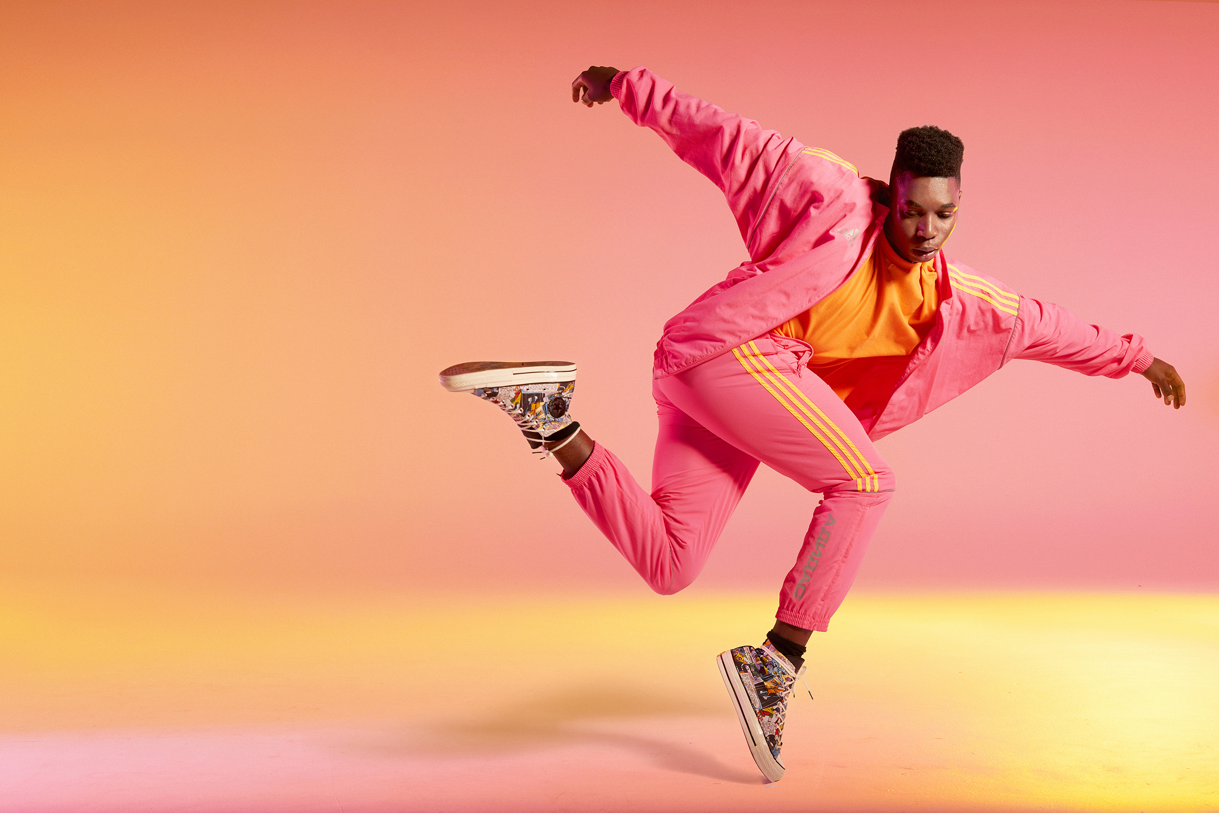 Young adult dances mid-air in pink tracksuit against gradient peach and pink background, showcasing athletic skill and dynamic pose.