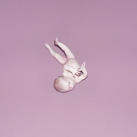 An infant baby positioned diagonally against a solid muted pink studio background, captured from an overhead perspective.
