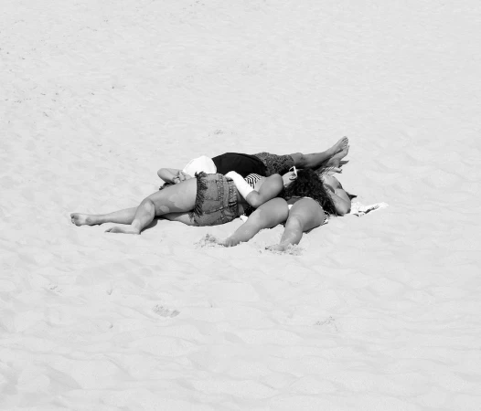 Two people lying closely together on a sandy beach under bright daylight