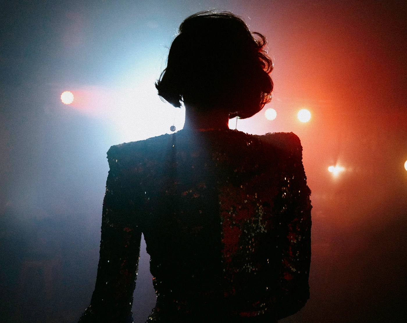 Silhouette of a woman with dark short hair wearing a sequined garment against stage lighting in Sydney by Juliet Taylor