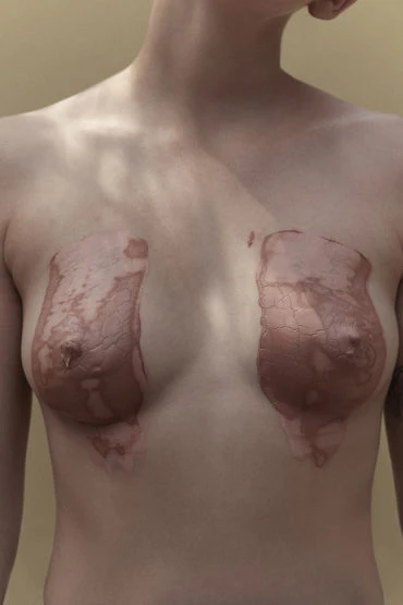 Artistic studio shot of a fair-skinned adult female torso with skin-tone body paint covering the breasts against a neutral background.